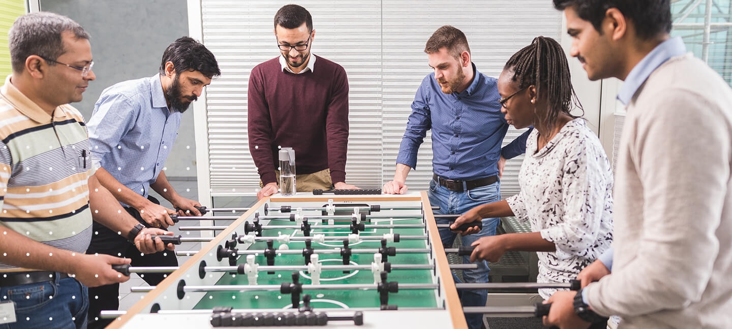 Six people playing foosball inside an office
